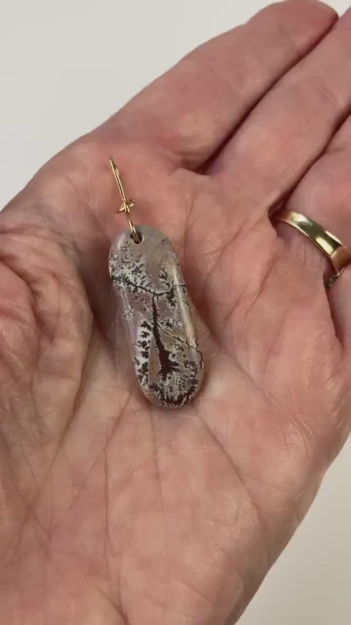 Dendritic Rhyolite Pendant with Gold-Filled Infinity Bail is shown in demo of pendant in a hand showing both sides of pendant.