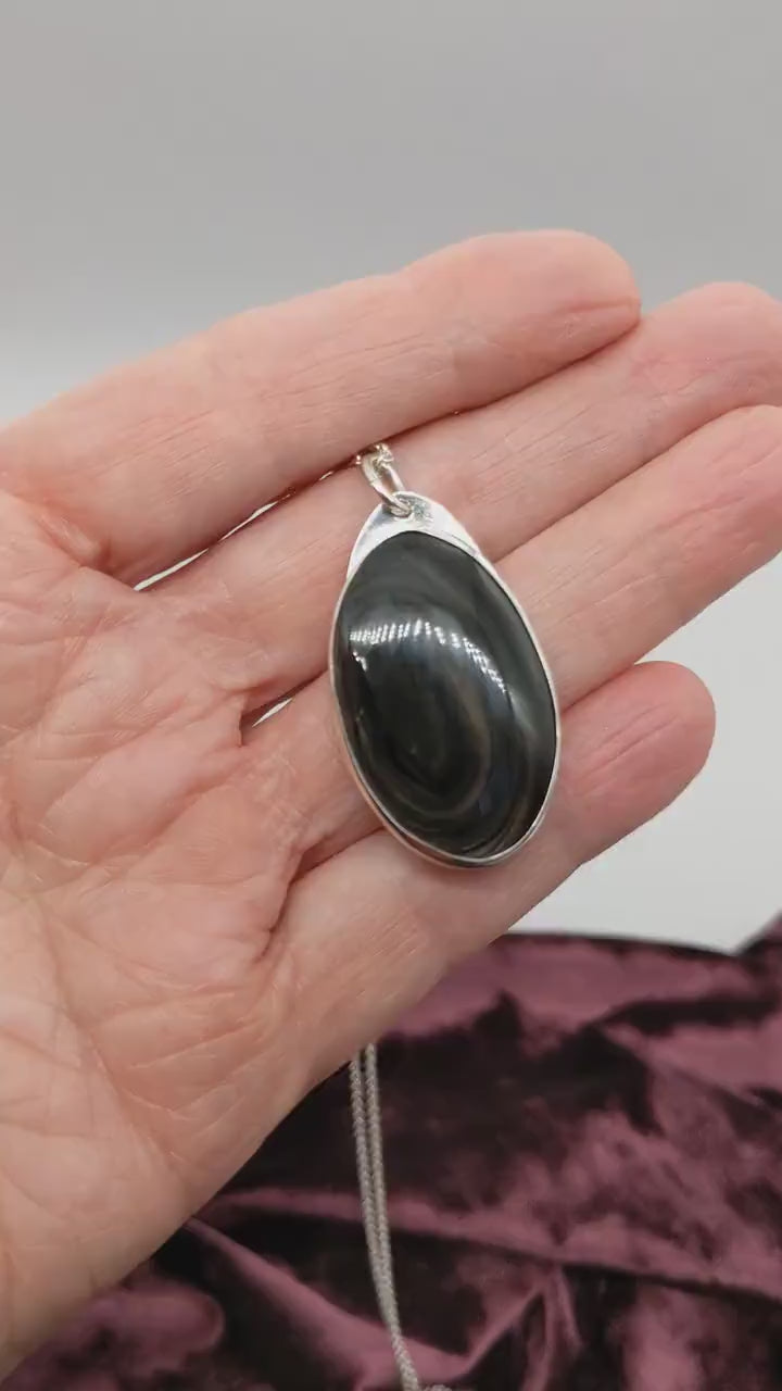 Demo clip of a  Mahogany Obsidian pendant displays swirling deep reddish-brown and dark mahogany hues, set in  Argentium® 935 Silver shown on white and burgundy background with silver necklace.
