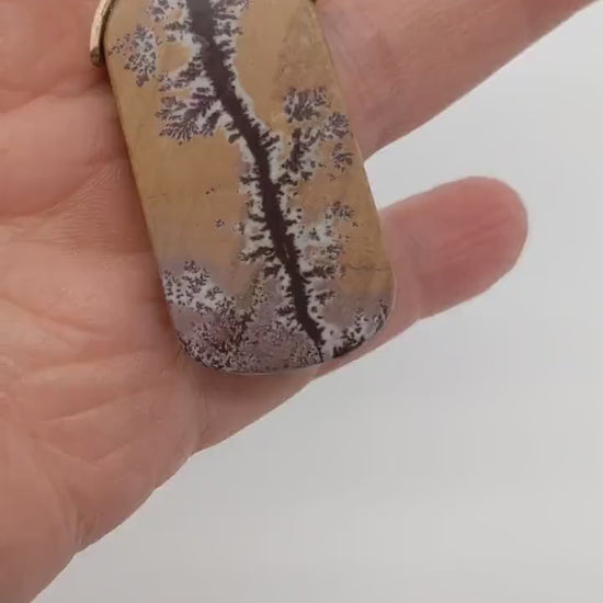 A demo video of a closeup of a one-of-a-kind Sonoran Dendritic Rhyolite Charm Pendant, hand-cut and polished to reveal the natural warm tan and soft pink hues accented by deep brown dendritic branch like patterns.