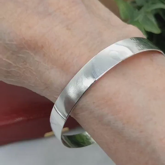Demo Clip of 9mm Bangle Bracelet, Crafted from 935 Argentium Silver, Features a Subtle Beveled Design shown on human wrist with red gift box and plant in background.