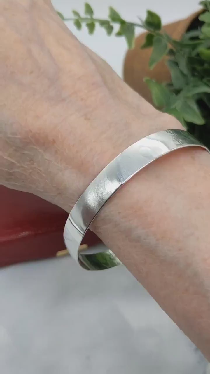 Demo Clip of 9mm Bangle Bracelet, Crafted from 935 Argentium Silver, Features a Subtle Beveled Design shown on human wrist with red gift box and plant in background.