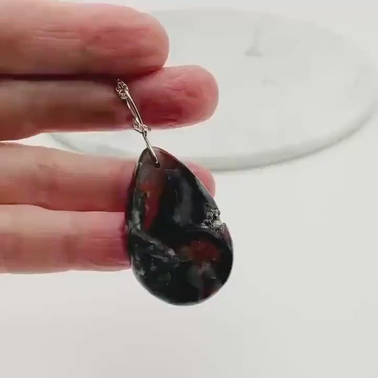Demo clip in hand showing closeup features of this Natural Mexican Red Agate druzy teardrop pendant with Argentium 935 Silver bail