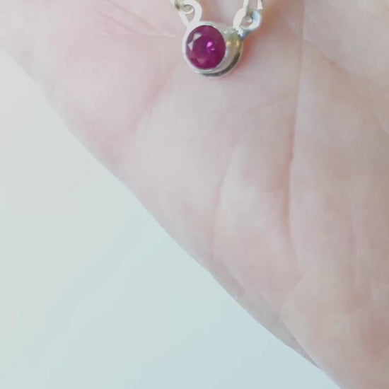 Demo of lab ruby pendant in Argentium Silver showing both sides in palm of hand against white background.