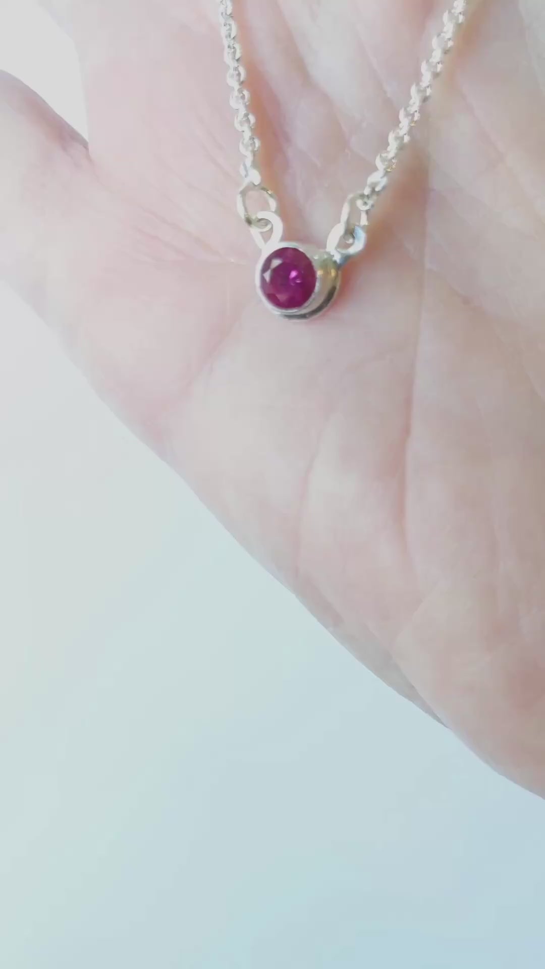 Demo of lab ruby pendant in Argentium Silver showing both sides in palm of hand against white background.