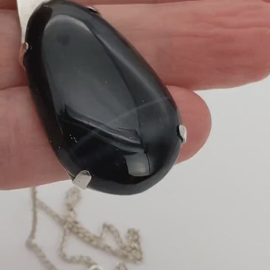 Demo of Handcrafted African Blue Tiger's Eye teardrop pendant with deep blue-black reflective gemstone, solid Argentium 935 silver tabbed setting and silver chain in a hand.