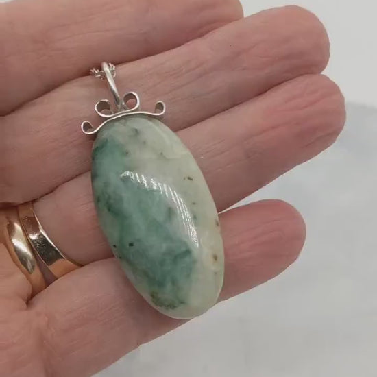 Demo clip in palm of hand to show the features of this African Turquoise Jasper pendant handcut polished on both sides for a reversible design. The stone reveals captivating hues of green and cream, reminiscent of natural turquoise, yet with its own distinct charm.  Set in a handcrafted bow-shaped bail made from tarnish-resistant Argentium® silver