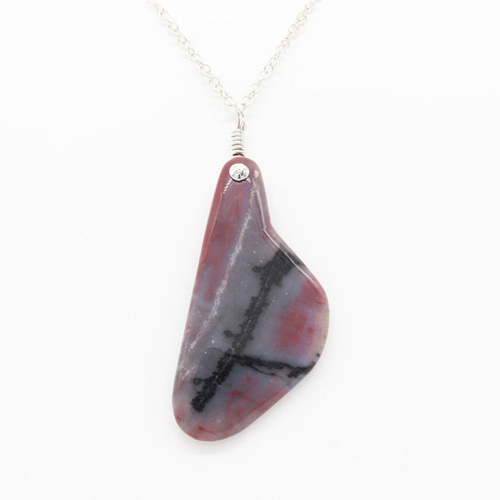Petrified Rainbow Wood demo of features of this pendant against background of white glove and light gray background.