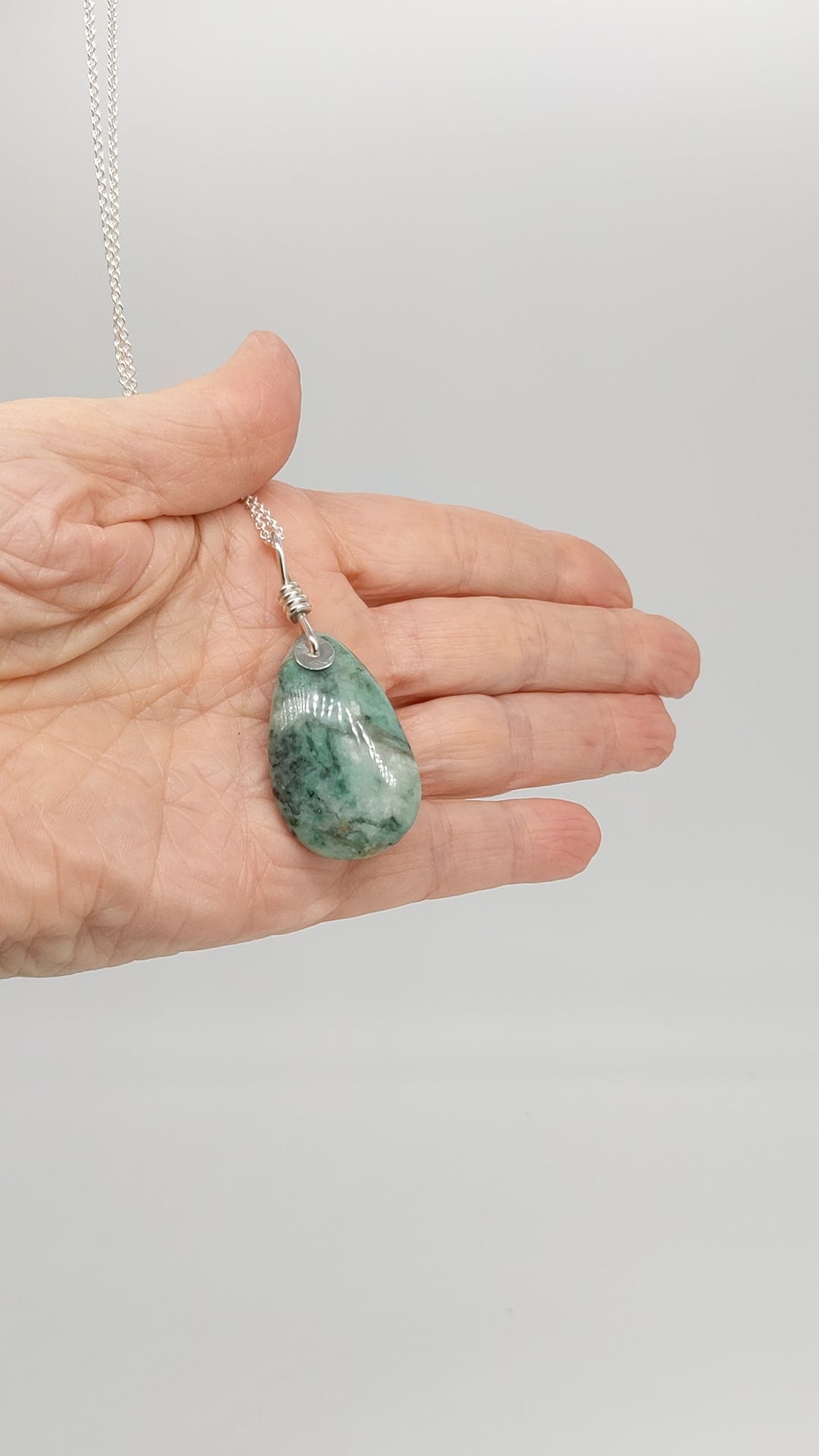 video of African Turquoise pendant shown in a hand displaying both sides with chain necklace.