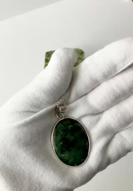 Demo Clip of Wyoming Jade pendant in palm of white gloved hand showing both sides and using a small light to highlight the translucent feature shown against light gray background.