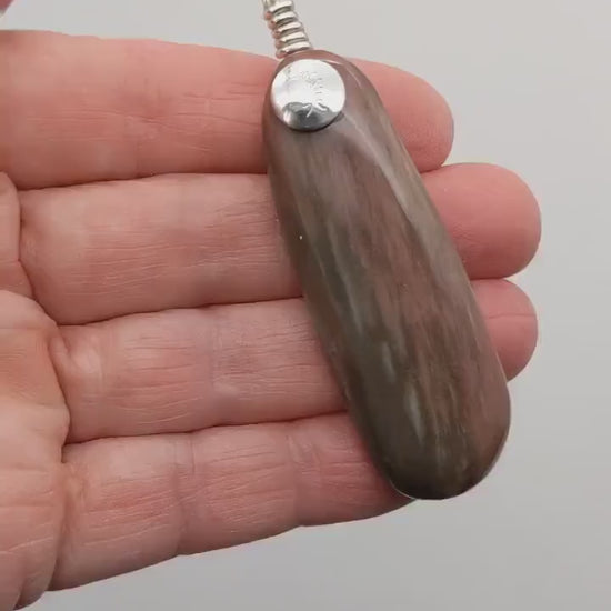 Demo clip of this Petrified Wood pendant with Argentium silver in the palm of the hand showing both sides of the pendant shown against a light gray background.