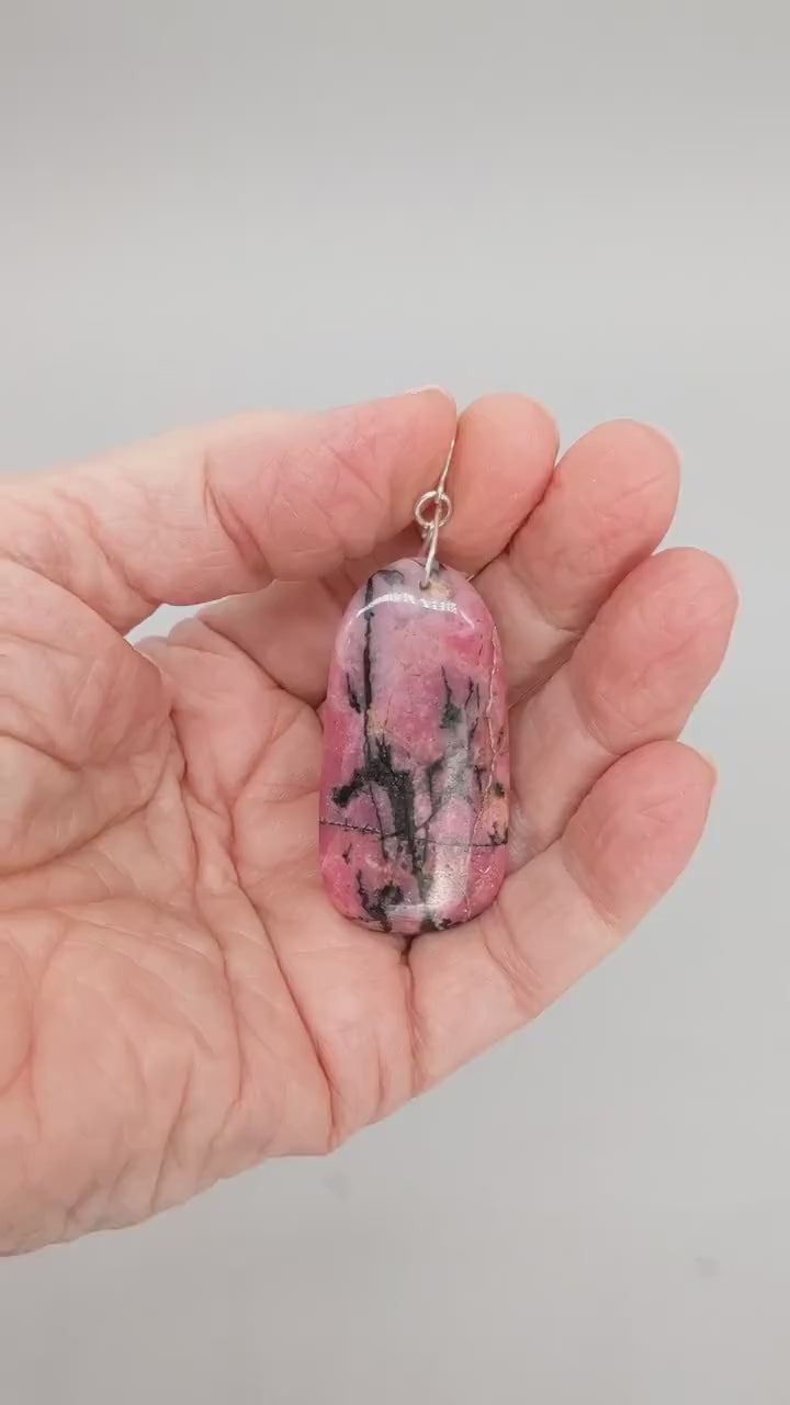 Demo clip showing both sides of the natural Rhodonite pendant in hand, with deep pink color and bold black veining.
