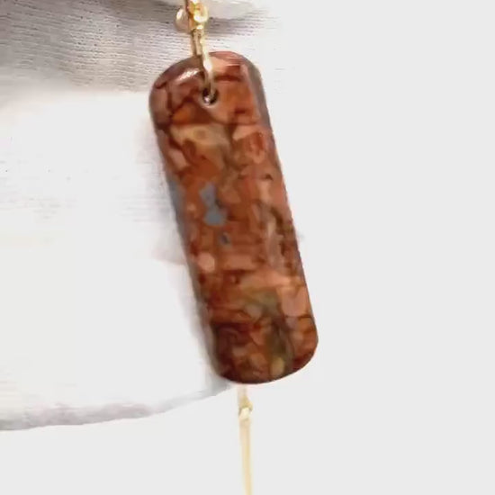 Demo of Stony Creek Jasper pendant  hand-cut and polished features bold red and deep blue patterns suspended from a handcrafted 14/20 Yellow Gold-Filled Infinity Bow Bail with optional Gold-Filled Rope chain against white glove background.