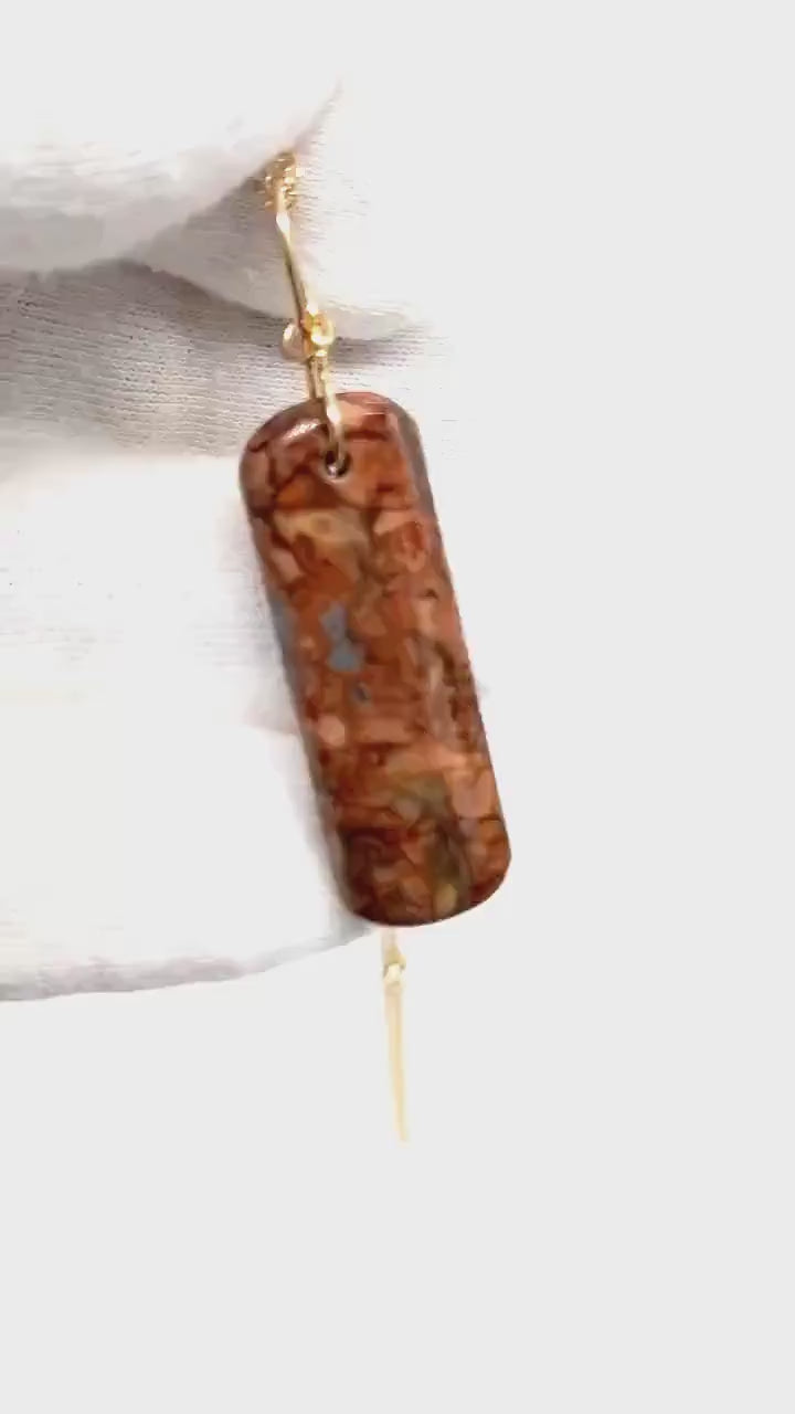 Demo of Stony Creek Jasper pendant  hand-cut and polished features bold red and deep blue patterns suspended from a handcrafted 14/20 Yellow Gold-Filled Infinity Bow Bail with optional Gold-Filled Rope chain against white glove background.