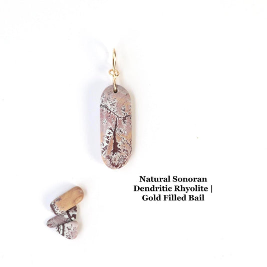A one-of-a-kind Sonoran Dendritic Rhyolite pendant charm. This natural gemstone from Mexico showcases warm tan and soft pink tones laced with delicate white and deep brown dendritic patterns—nature’s own artwork.  Finished with a custom 14/20 gold-filled infinity bow bail.