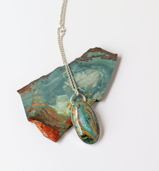 Necklace with a Sonoran Jasper pendant next to raw Sonoran Jasper rock against  white background.