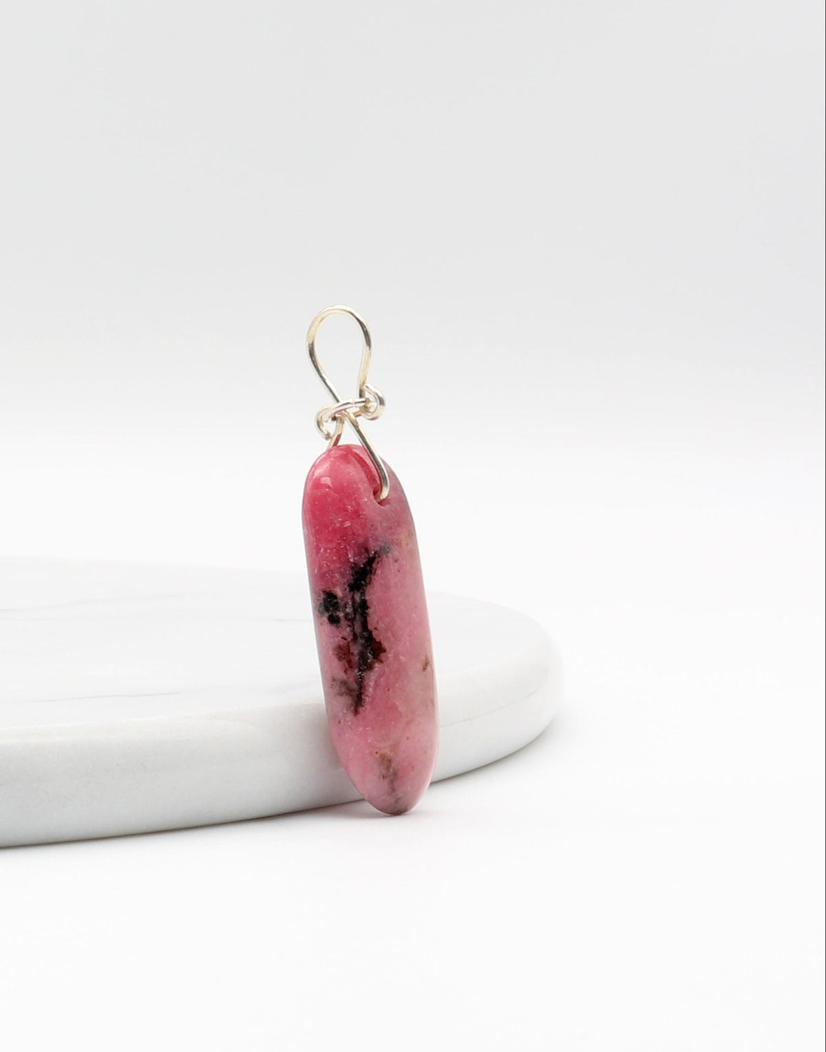 Side view of this natural pink Rhodonite pendant with black inclusions, shown next to a white marble slab.