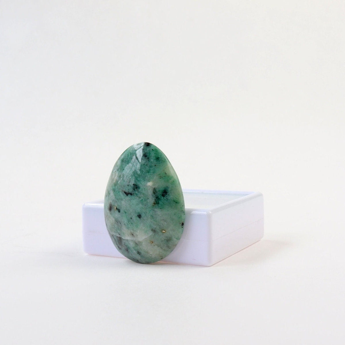 Hand-cut African Turquoise Jasper teardrop cabochon with natural teal-green, cream, and dark mineral patterning shown at right angle next to white gem box on a white background