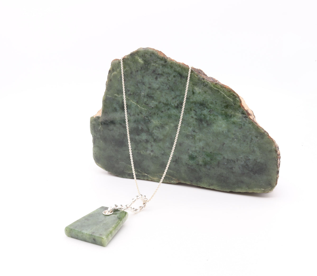 A silver chain necklace with a rough Wyoming rock next to finished pendant,  on a white background.
