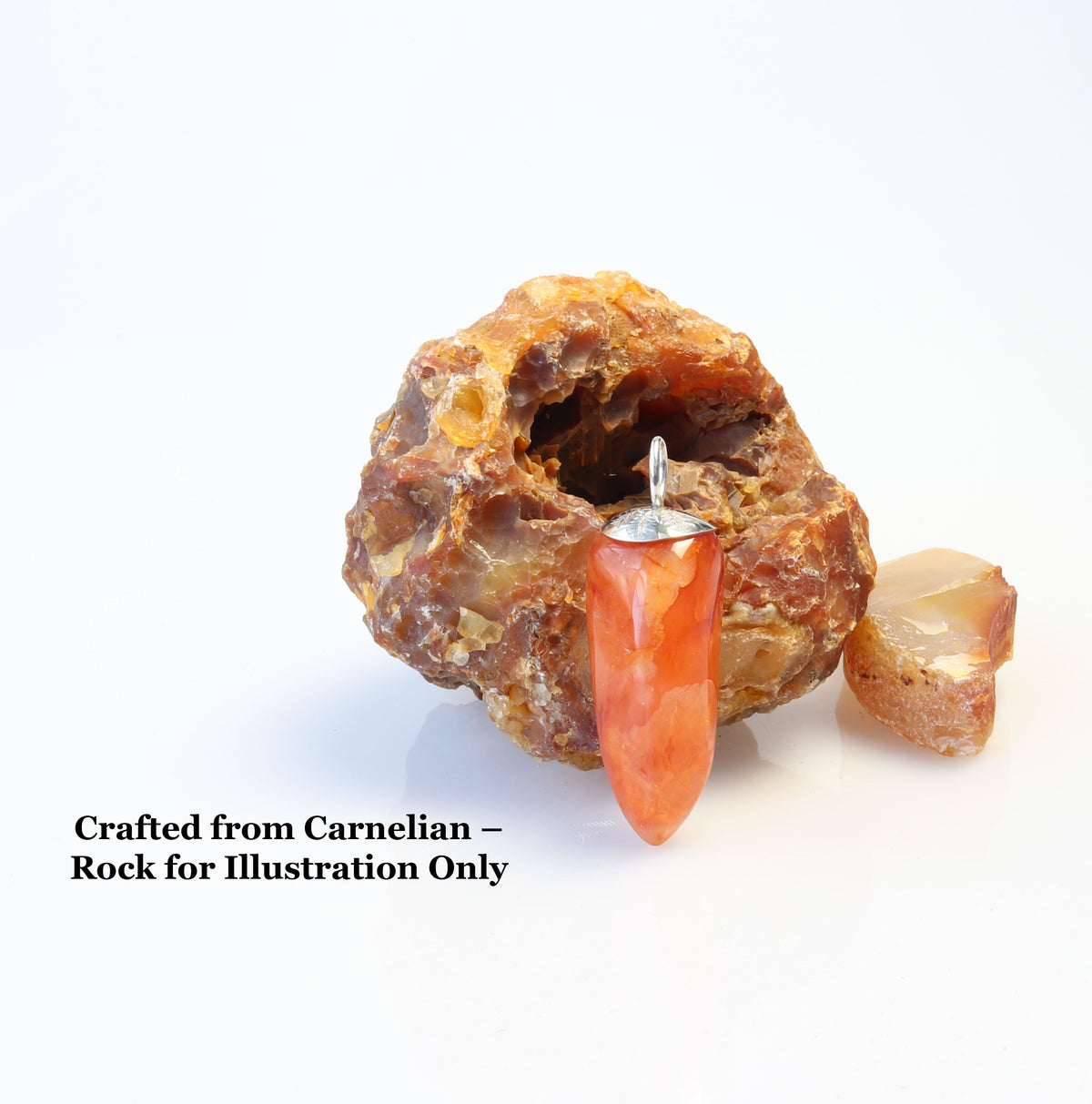 Handcrafted Carnelian Agate pepper-shaped pendant with Argentium 935 Silver bail, 54.81mm, standing adjacent to a raw Carnelian rock (for illustration only, not for sale) on a light background