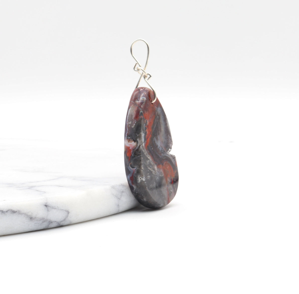 Natural Mexican Red Agate druzy teardrop pendant with Argentium 935 Silver bail  and resting on a white marble slab against a white background.