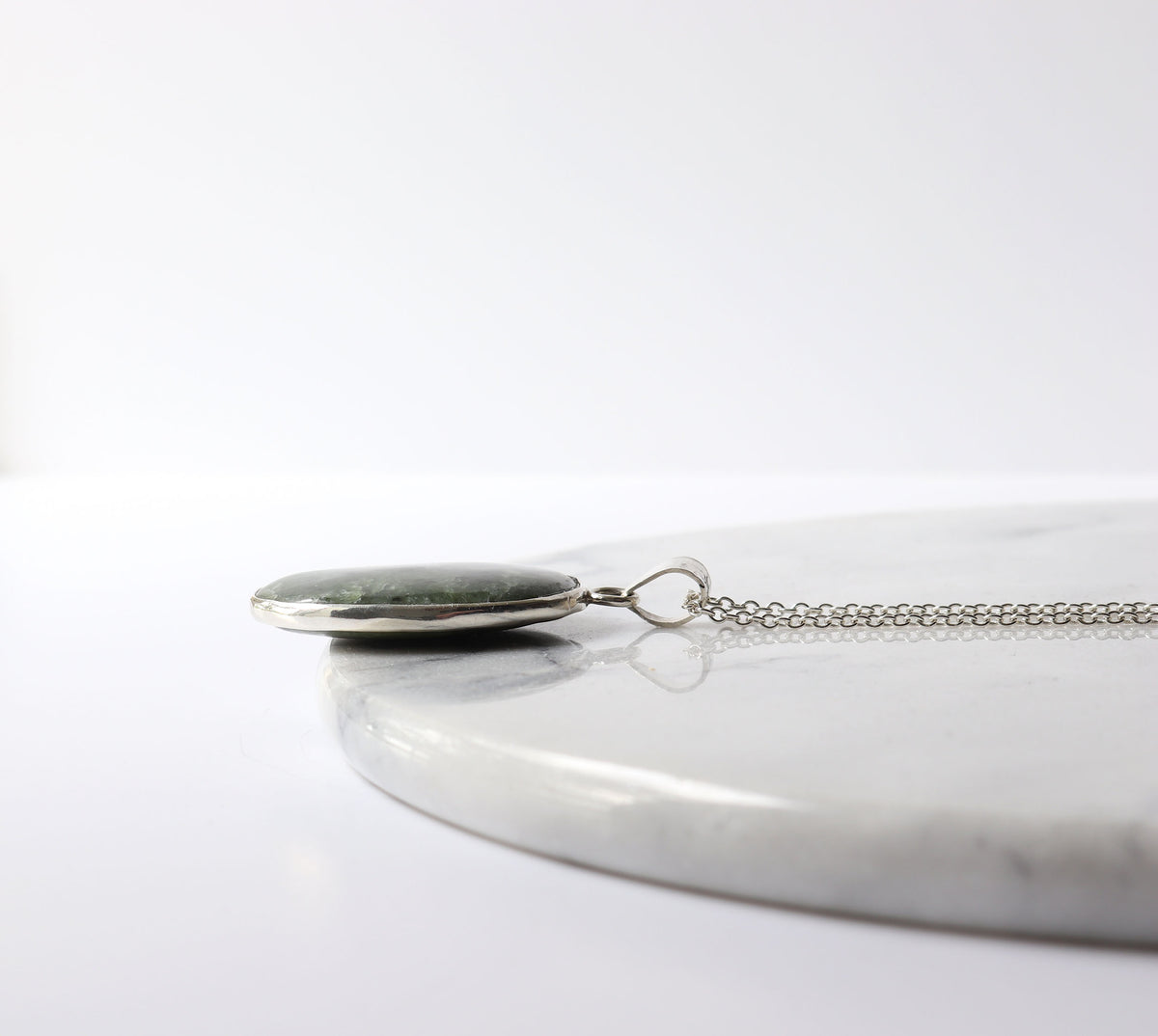 An Open, ring-supported Argentium® Silver setting with both sides of the Wyoming jade visible, resting on a white marble slab against a clean white background.
