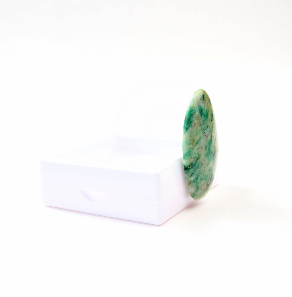 A side view of this hand-cut Mariposite oval cabochon with green and creamy white natural pattern, standing against white gem box and displayed on a clean white background.