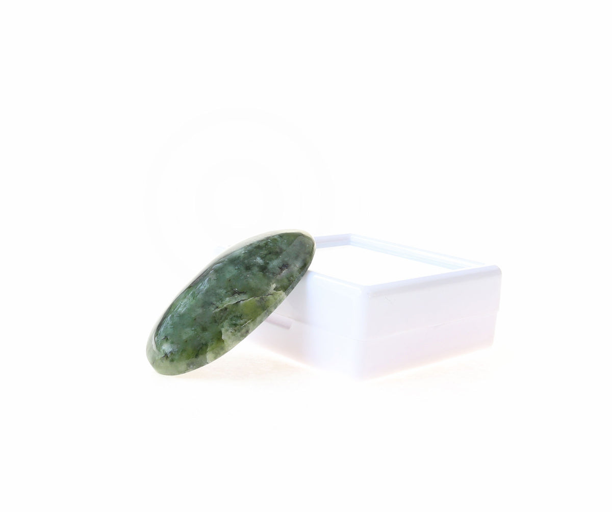 A polished Wyoming Jade stone cabochon leaning at an angle against a small white rectangular gem box, photographed on a clean light gray background.