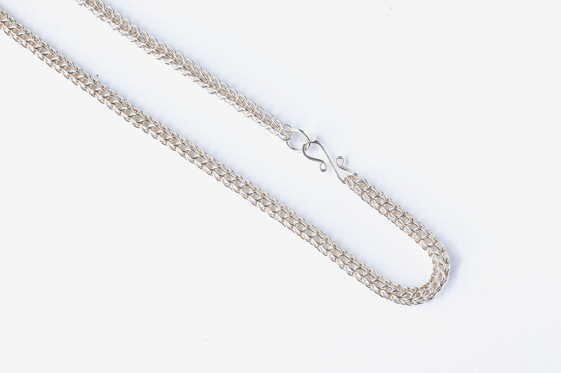 Closeup of S-Hook clasp and 6 and 1 Persian weave necklace.  Silver chain necklace on a white background