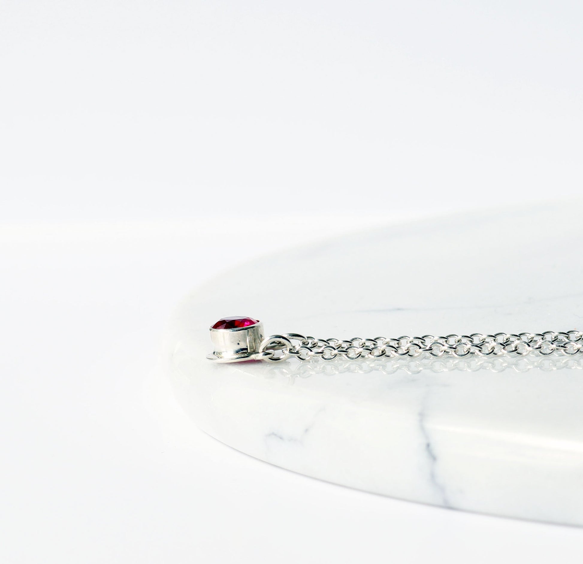 Side view of 6mm round faceted lab-grown ruby in a custom Argentium® Silver bezel setting.