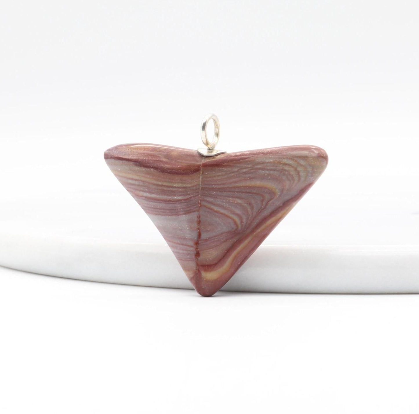 A handcut polished Butterfly Shaped Petrified Rainbow Wood pendant features earthy tones of deep crimson, purple, and tangerine with handcrafted Argentium 935 silver bail shown against white marble slab and white background.
