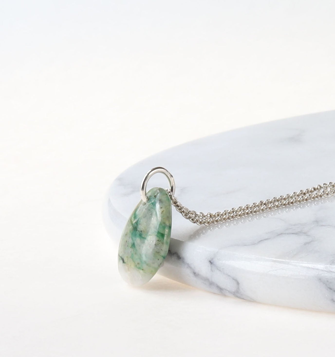 Necklace with a mariposite pendant on a marble surface against light gray background.