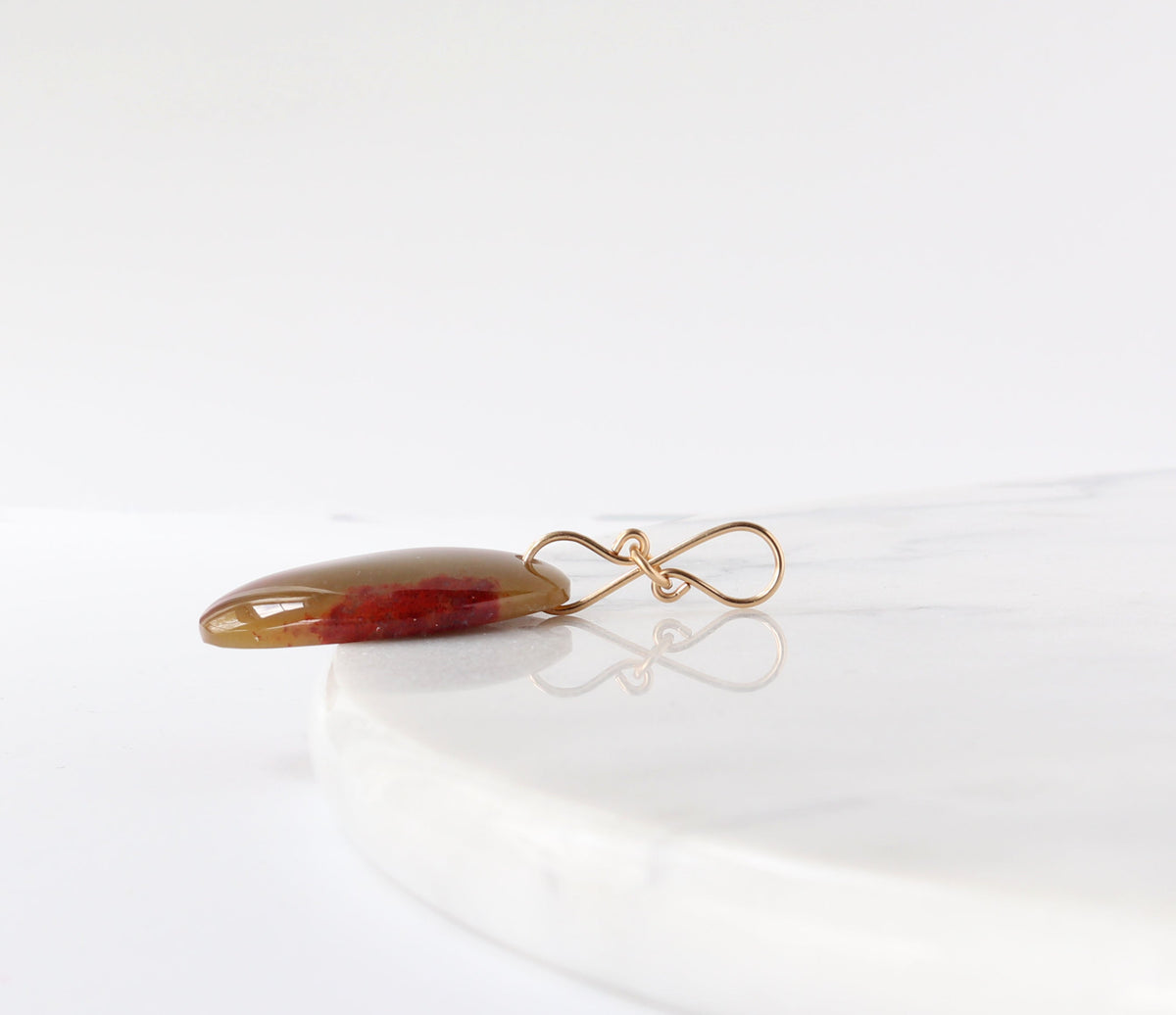 Side view of sonoran sunrise pendant shown on white marble slab against white background.