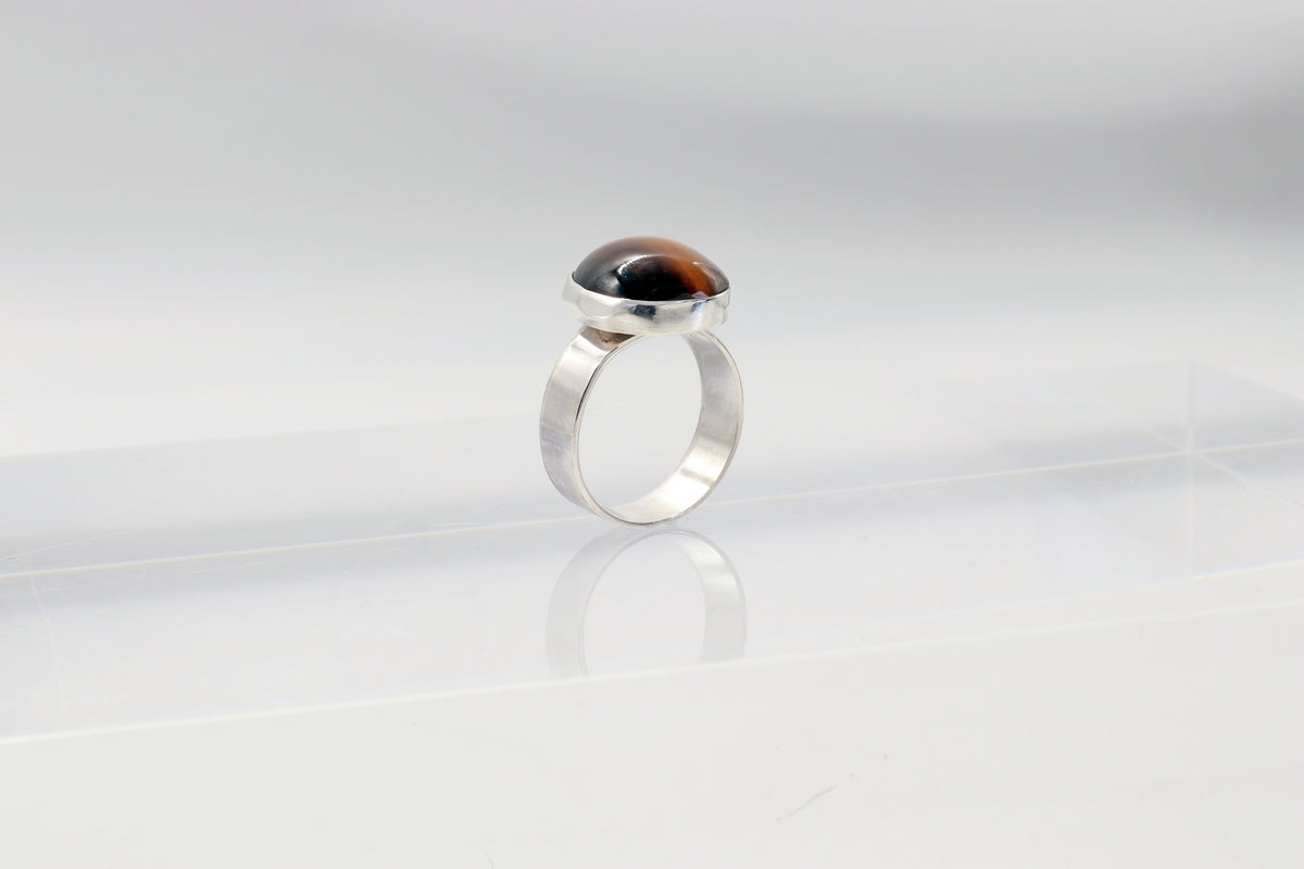 Natural Tiger's Eye ring in solid Argentium 935 silver shown standing on a light gray background.