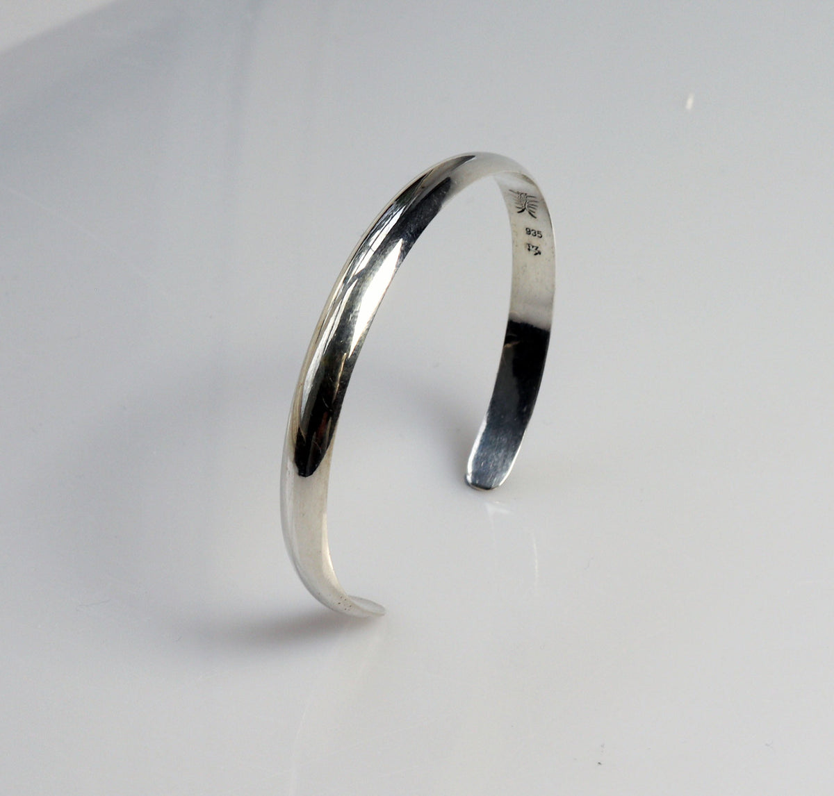 Argentium Silver Cuff handmade low dome style shown standing side-angle shows the low-dome cross-section and curvature  on light gray background with makers mark and 935 stamp.