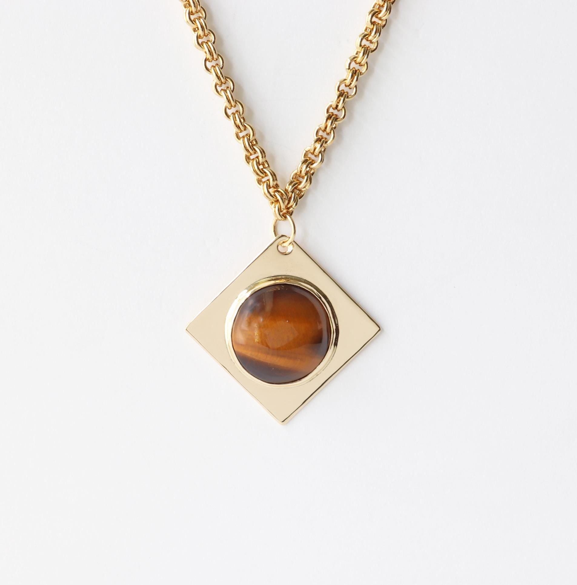 A closeup of a 1.625 Tiger’s Eye pendant, featuring a .75” round cabochon set in a four-point diamond-shaped NuGold brass setting. This one-of-a-kind artisan pendant is hand-cut and polished in our Missouri studio, ensuring a high-quality, handcrafted component for your custom jewelry designs.  Shown against white background with double-link brass chain sold separately.