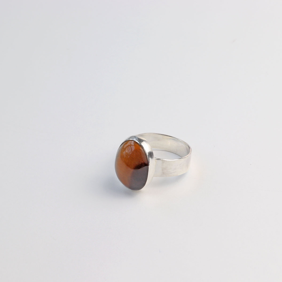 Natural Tiger's Eye ring in solid Argentium 935 silver shown on light gray background.