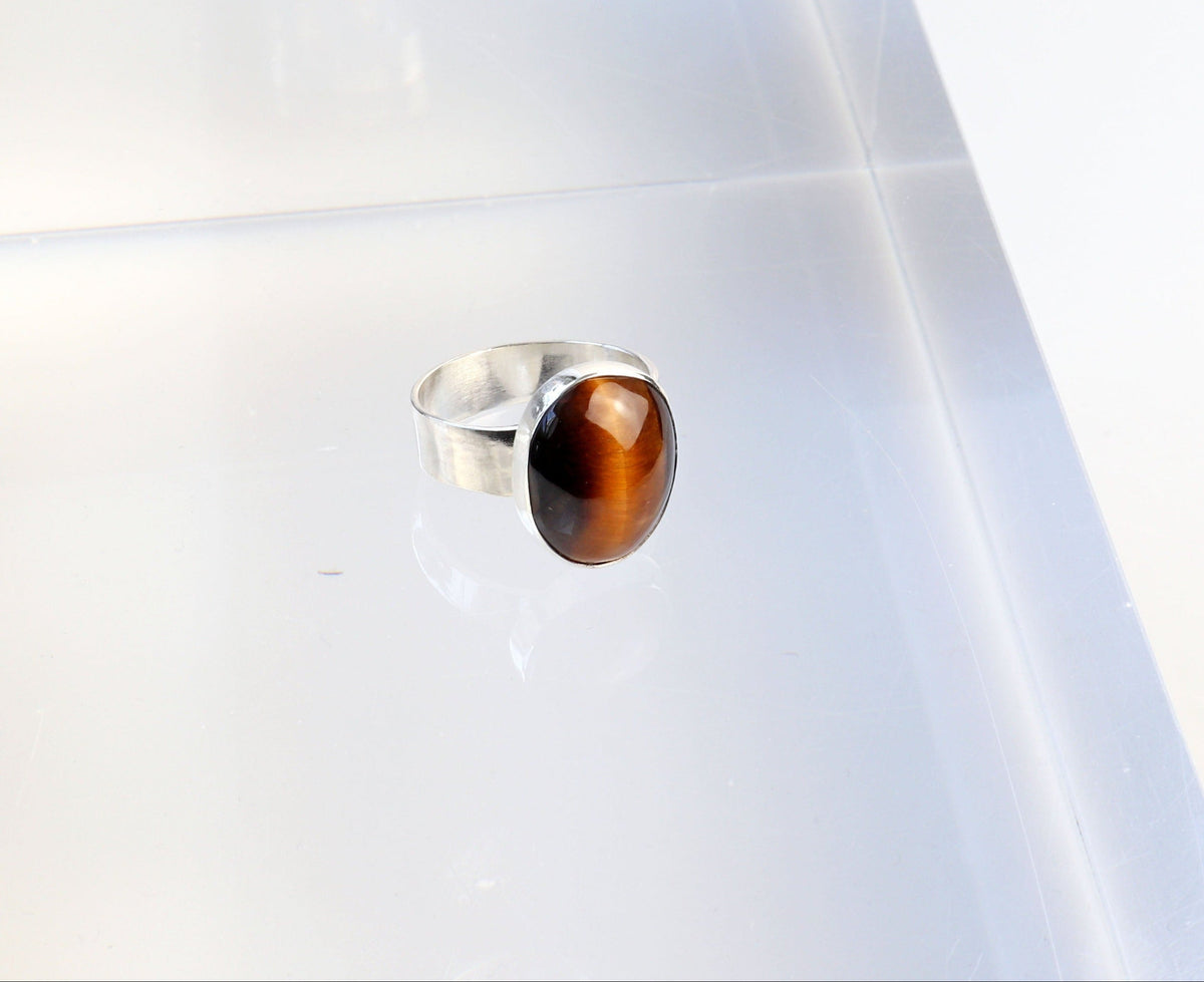 Natural Tiger's Eye ring in solid Argentium 935 silver shown on acrylic block on light gray background.