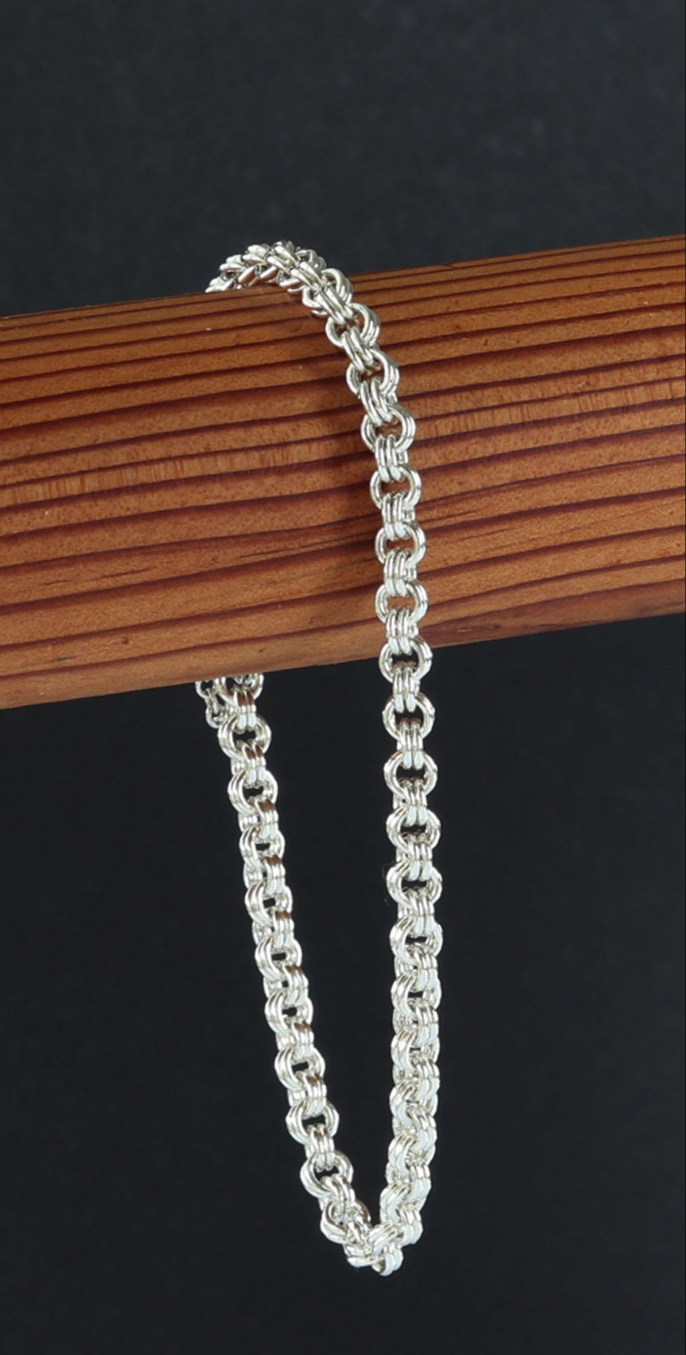 Argentium Silver handcrafted Double cable chain bracelet on a wooden stick against a black background