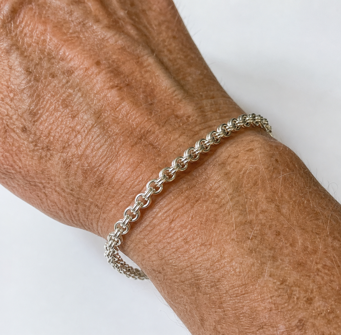 Wrist with Argentium double link cable chain on white background.